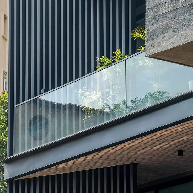 A balcony edge with a frameless glass railing against dark timber cladding