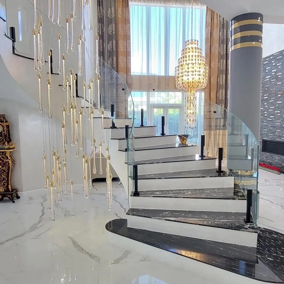 A curved staircase with a frameless glass railing under a hanging light
