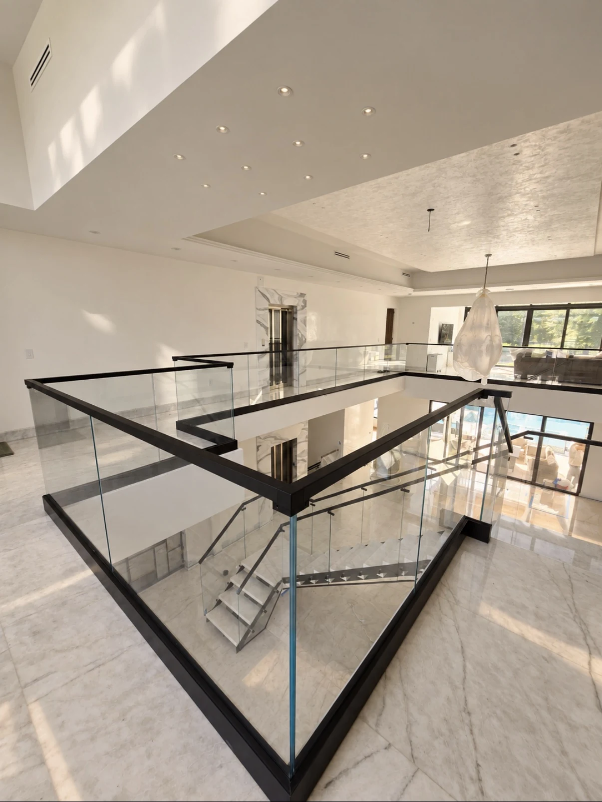 An open mezzanine edged with frameless glass and a black top rail, the room below visible through it