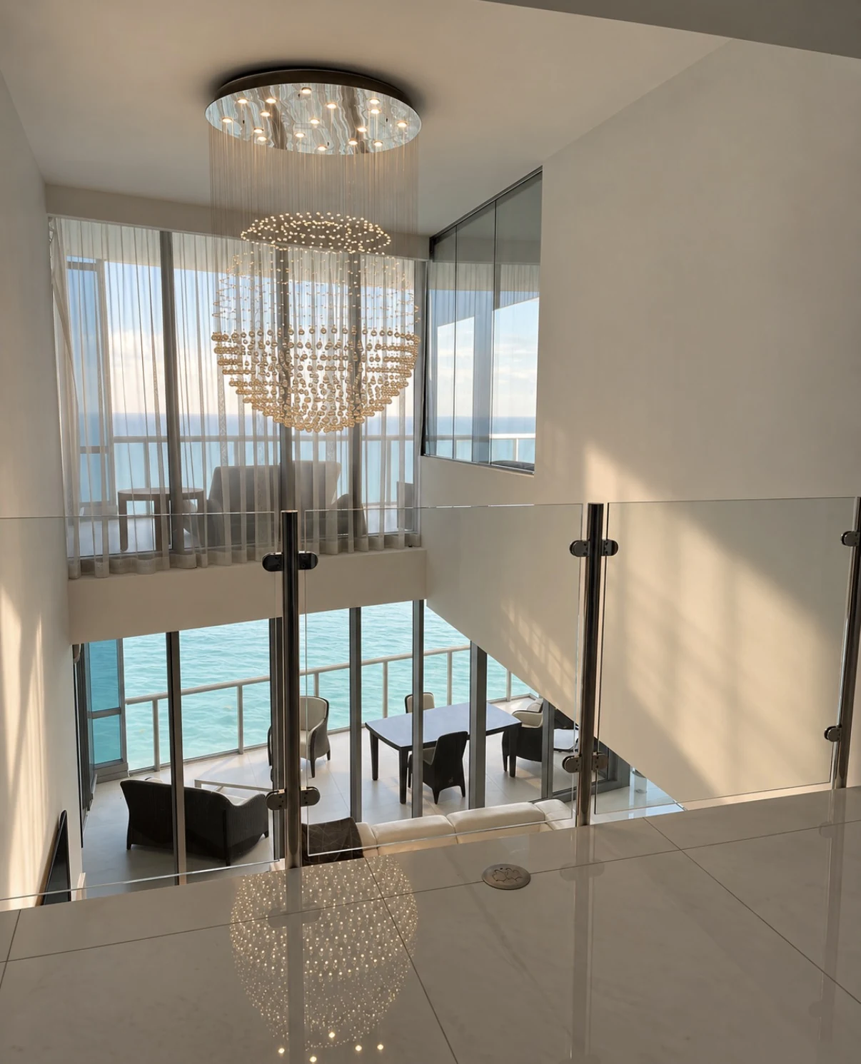 A landing behind a frameless glass railing in an oceanfront apartment, daylight from the windows beyond